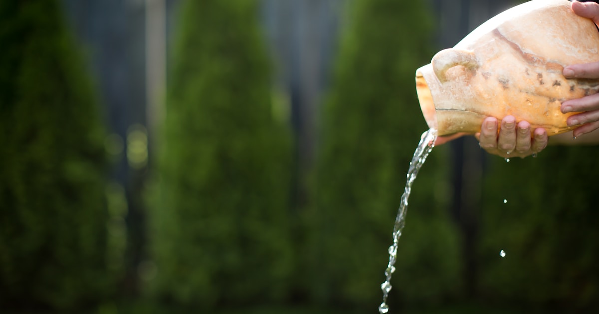 Женщина пьёт воду из стеклянного стакана на фоне природы, символизируя здоровый образ жизни и заботу о гидратации организма.