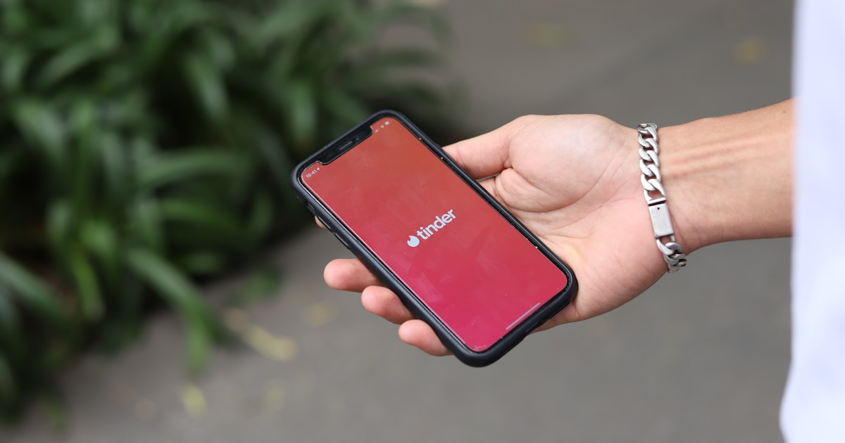 Экран смартфона с открытым приложением Tinder на фоне тематики Супербоула